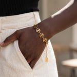 Adinkra Charms Gye Nyame gold bracelet featuring ten symbolic charms on a stainless steel chain worn on a wrist.